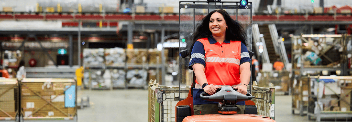 Warehouse team member driving a tugger across facility floor with facility in background.