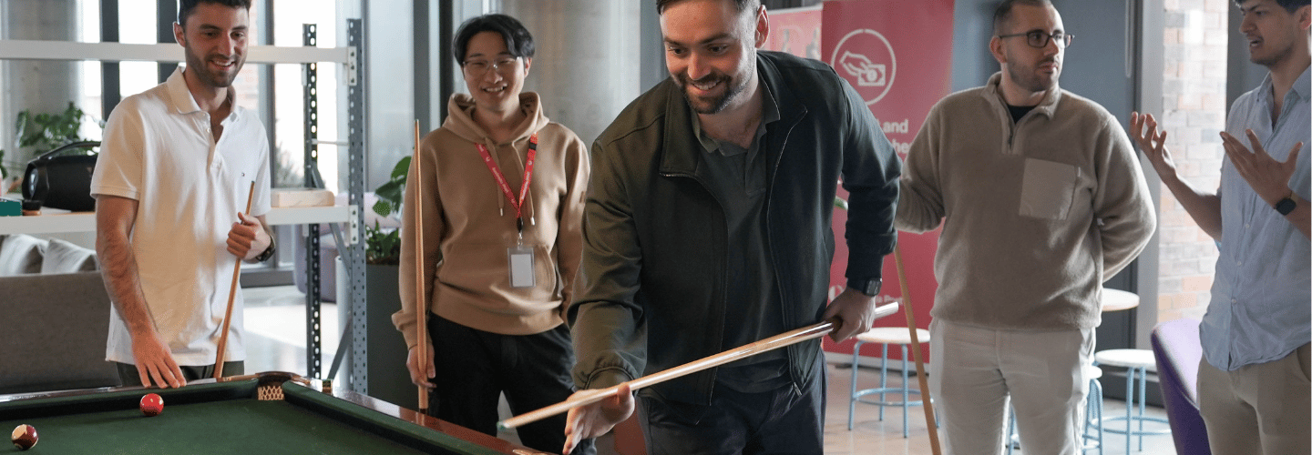 A group of team members smiling and playing a game of pool together in the office