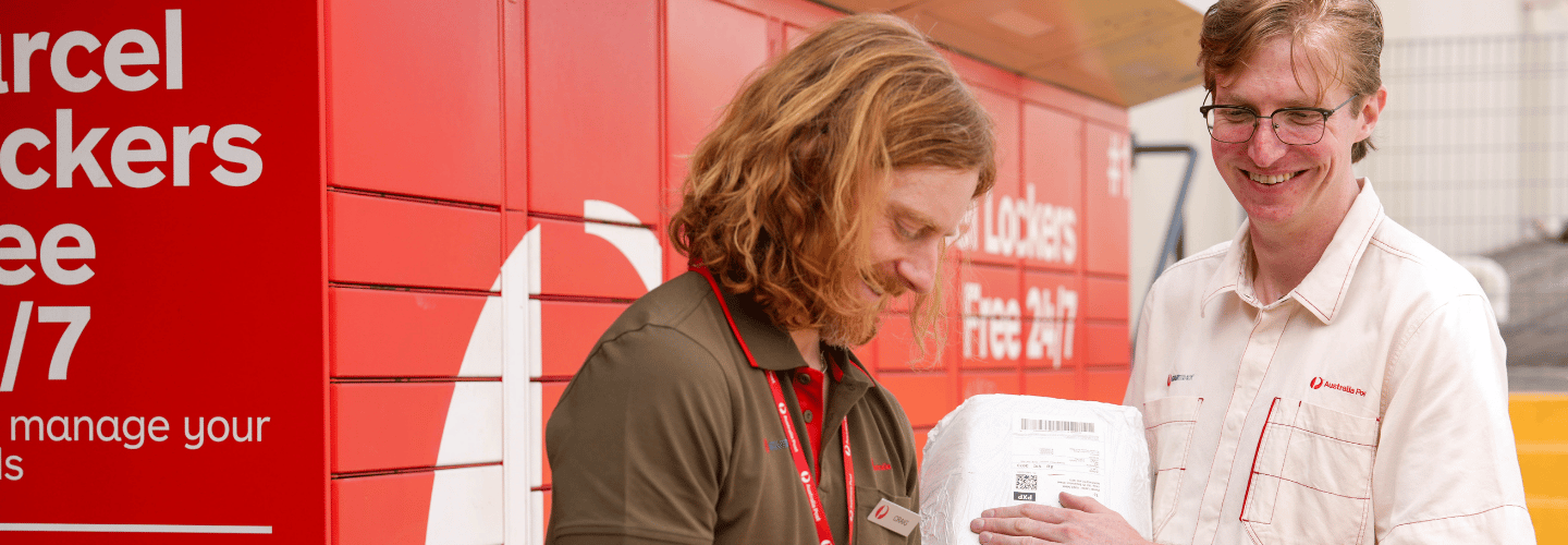 Retail team members standing outside scanning parcels in front of an Australia Post parcel locker
