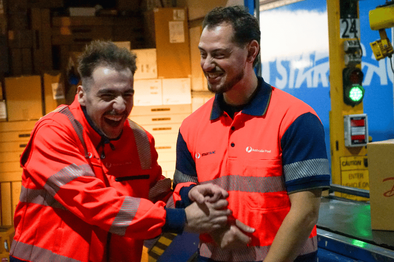 Two team members in hi-vis standing outside of a StarTrack truck laughing a joking together