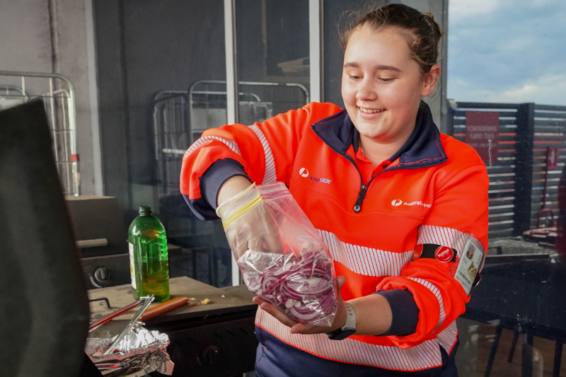 Facility team member standing at a BBQ and reaching into a bag of cut up red onions in preparation to cook them