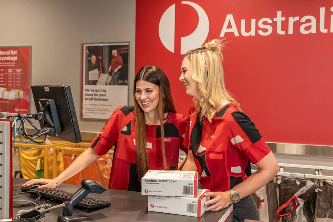 A retail team member smiles, walking past Postal Lockers and Post Boxes.