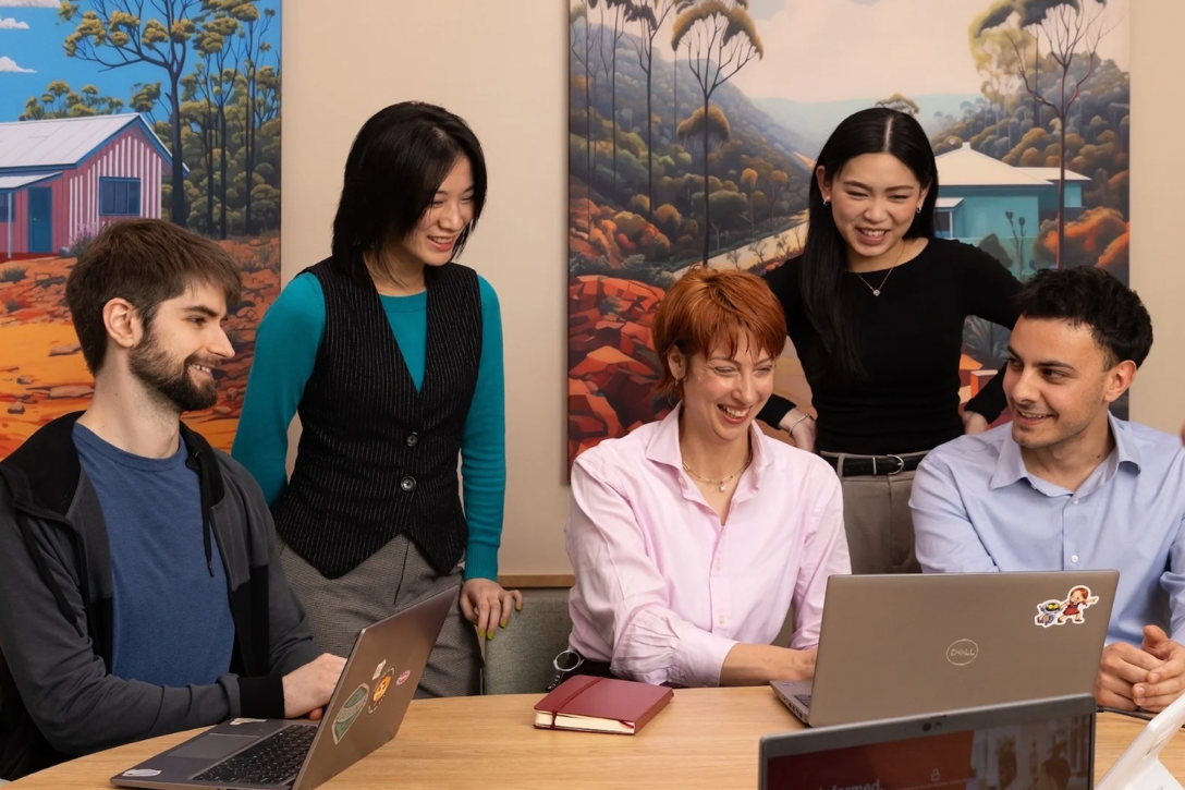 Two office team members working on laptops smile to the camera.