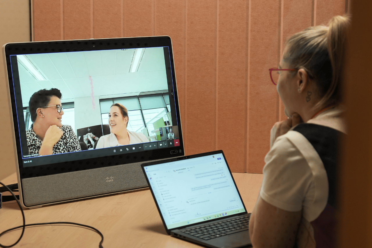 Team member sitting in a meeting room talking to two colleagues virtually via video call