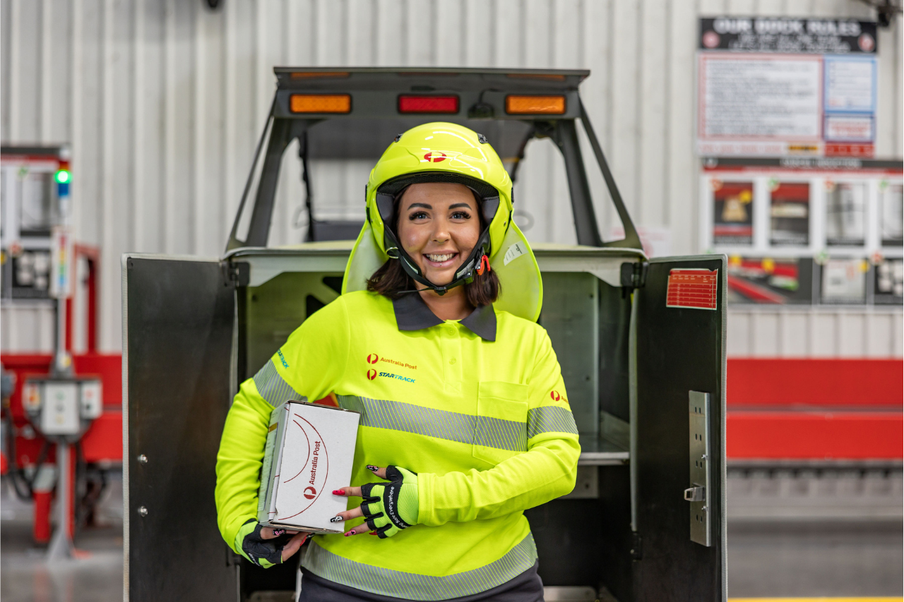 Postie in uniform packs EDV with mail while smiling to the camera.