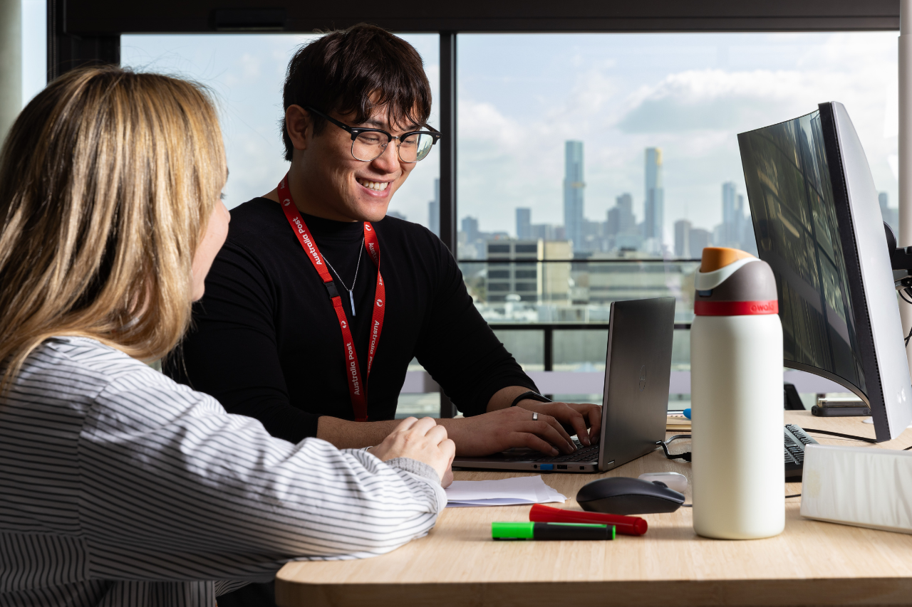 Office team member in a black shirt sitting in front of a laptop laughing.