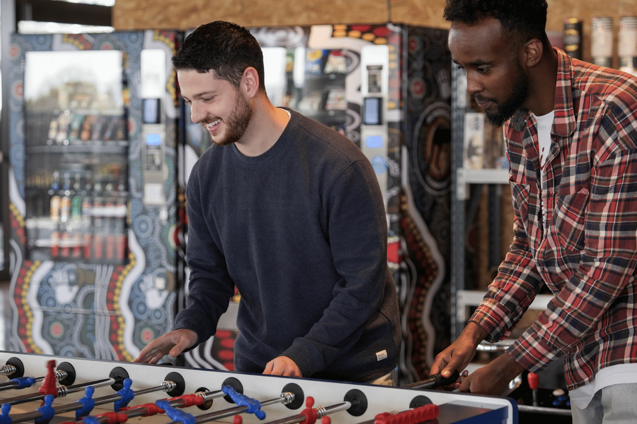 Two team members play at a foosball table together laughing.