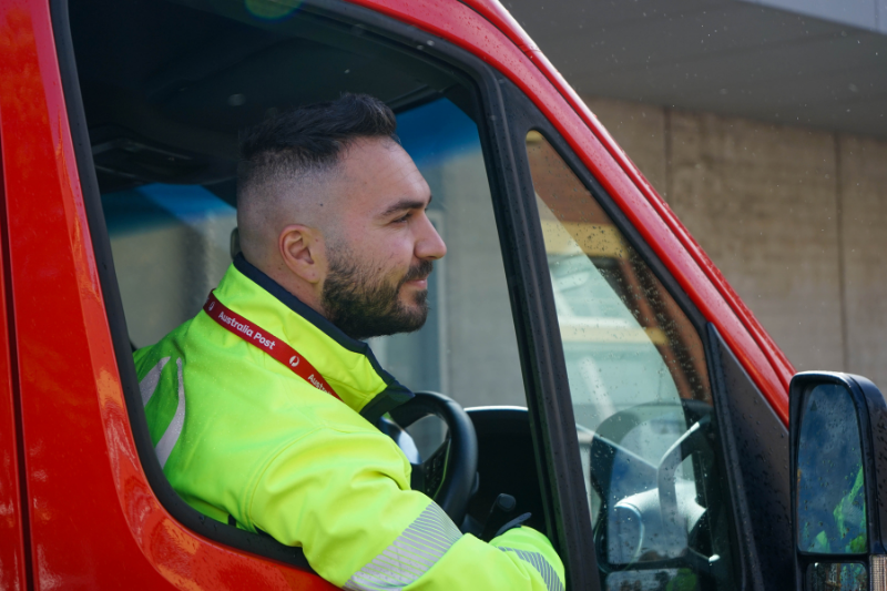 Van driver sitting in a red van leans out of driver’s side window looking at the road ahead.