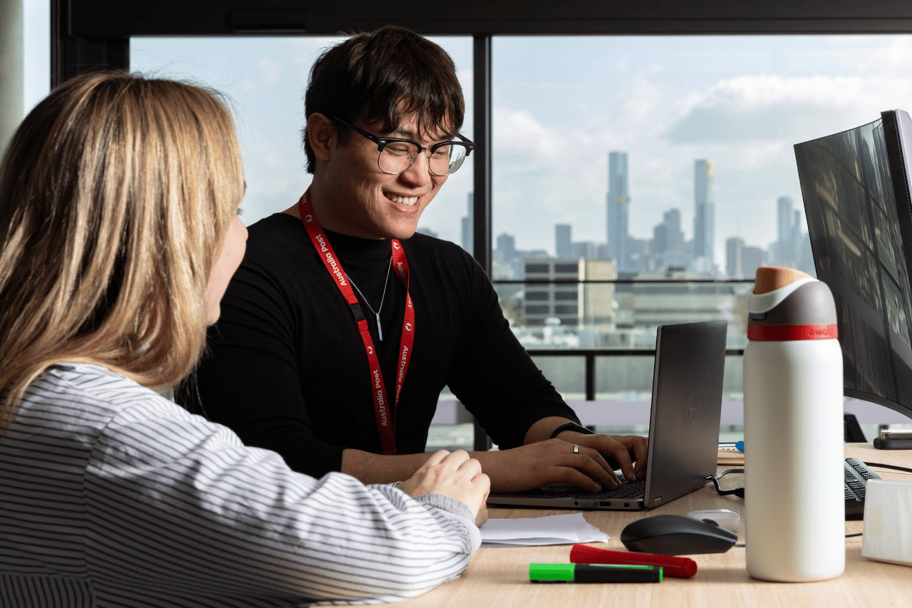 Office team member talking to a colleague at a standing desk with a view of the city in the background