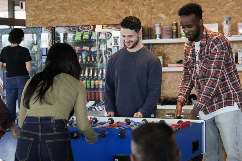 A group of team members smiling and playing a game of foosball together in the office