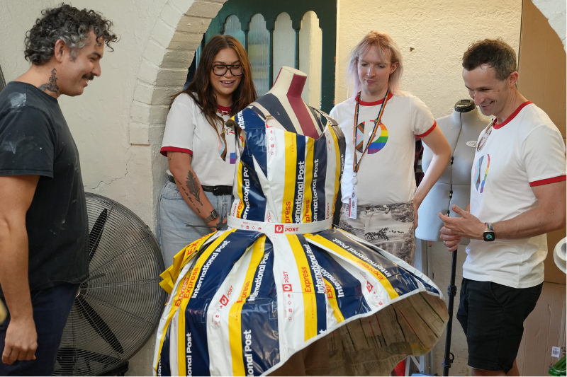 A group of team members and drag queen Vin Tage in Pride shirts standing behind a mannequin featuring dress made from AusPost satchels