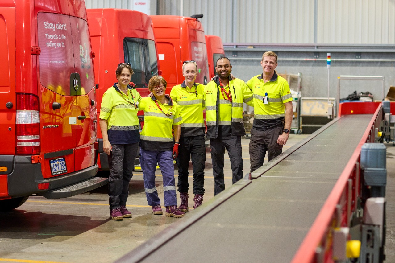 Five warehouse team members in uniform stand together smiling to camera.