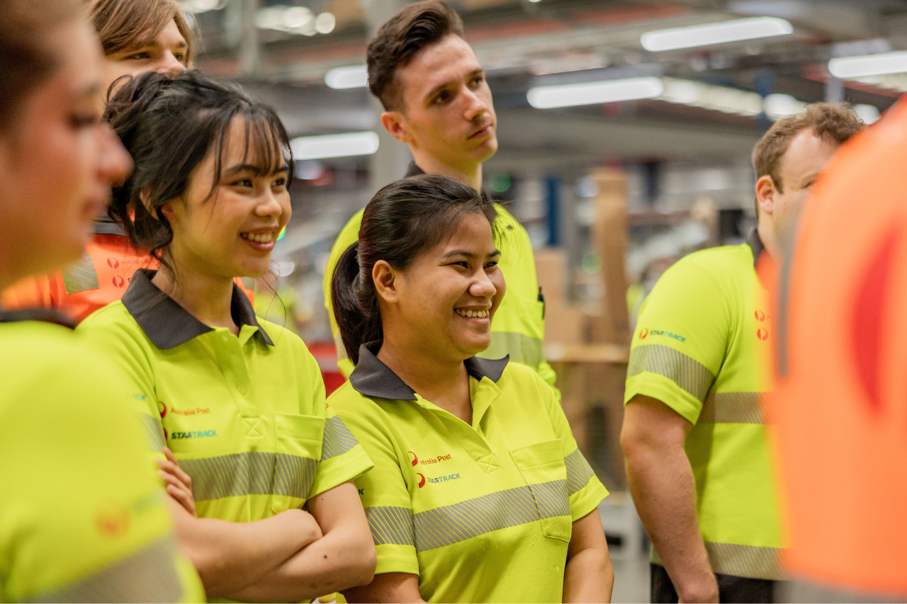 Five warehouse team members in uniform stand together smiling to camera.