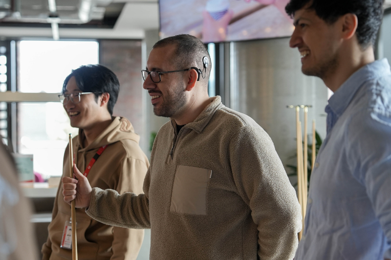 Team member with cochlear implant standing with teammates holding a pool cue