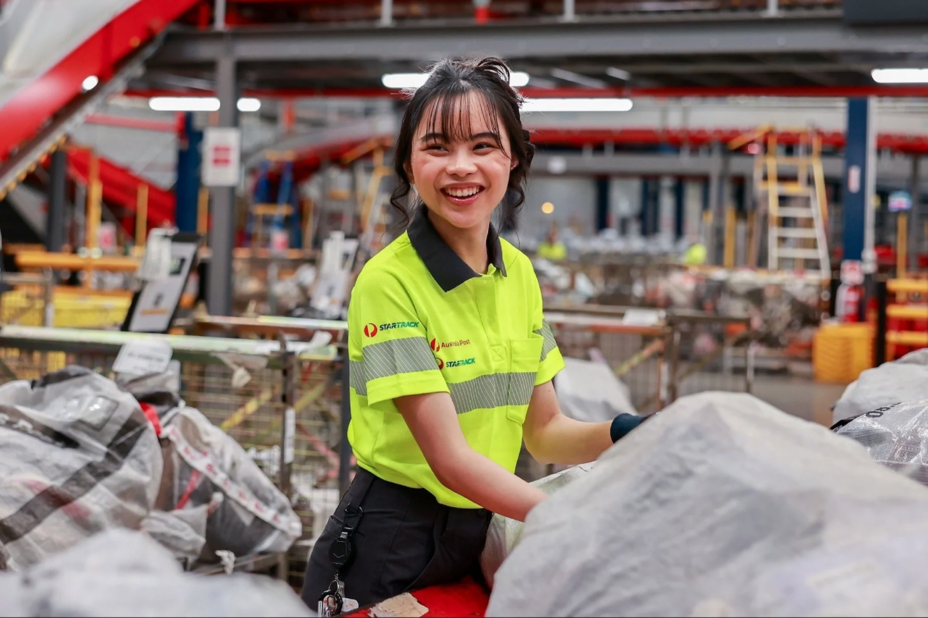 Mail processing team members chat while working beside conveyor belt.